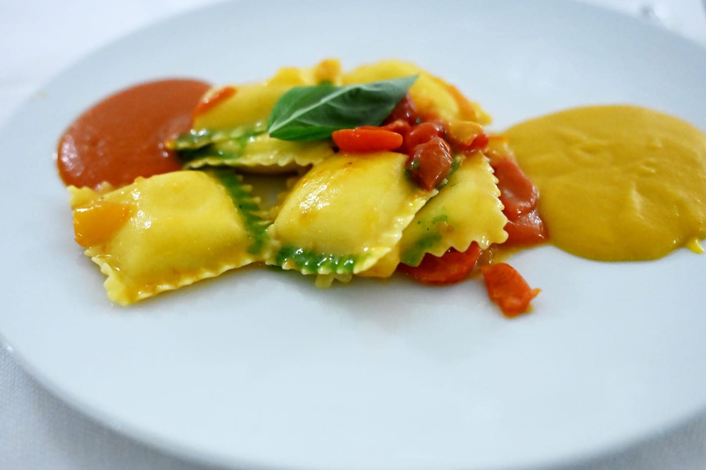 Ravioli serviti su due salse con basilico fresco